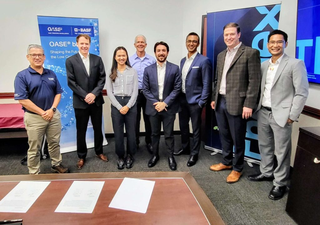 Group of professionals at a BASF and OASE event with promotional banners in the background, signing documents on the table.