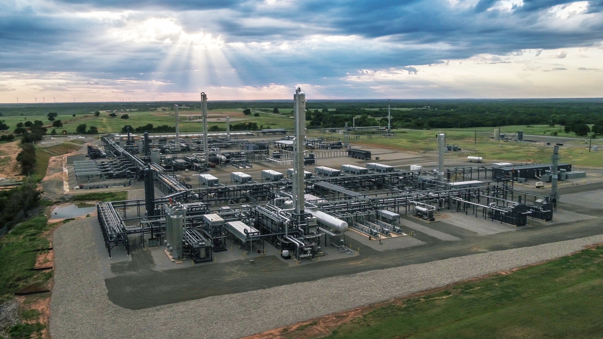 Aerial view of a large industrial plant with complex piping system in a rural landscape under a cloudy sky.